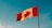A Canadian flag waves against a clear blue sky. The flag is prominently featuring the iconic red maple leaf centered on a white background, flanked by red vertical stripes on either side.