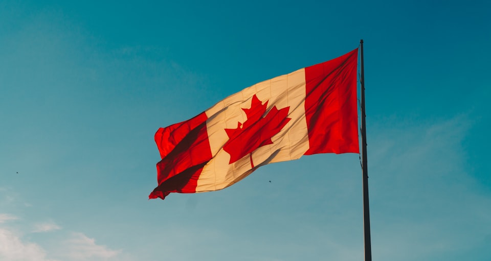Photo of a Canadian flag in the wind against a clear sky.