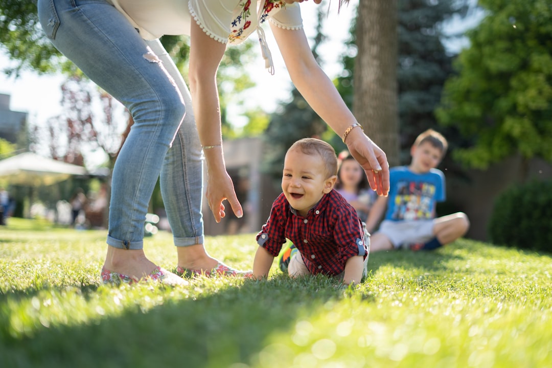 woman in white blouse and blue denim jeans helping a baby crawl on green grass