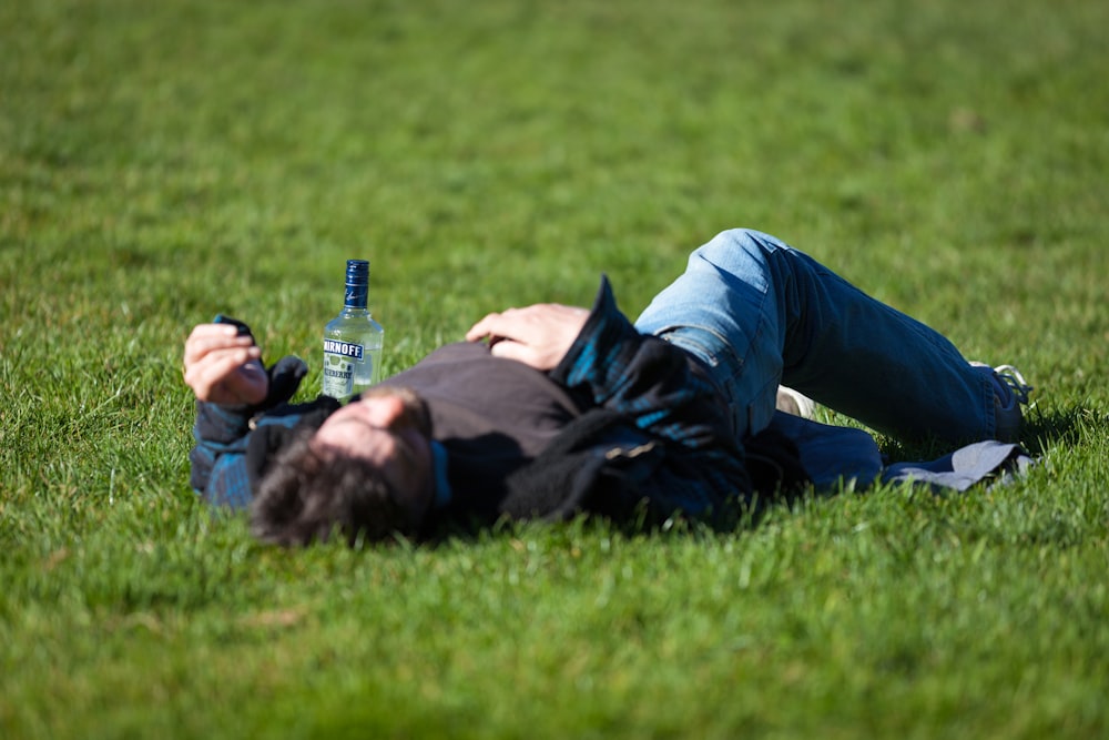 a man laying in the grass with a bottle of beer