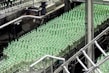 A production line filled with rows of clear plastic bottles capped with green lids. The bottles are neatly organized and moving along a conveyor in an industrial setting, indicating a bottling plant or factory environment.