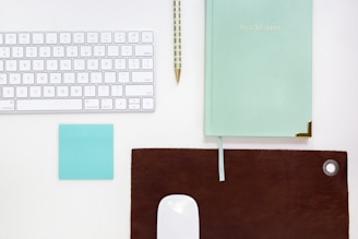 green book beside ballpoint pen and Apple magic keyboard