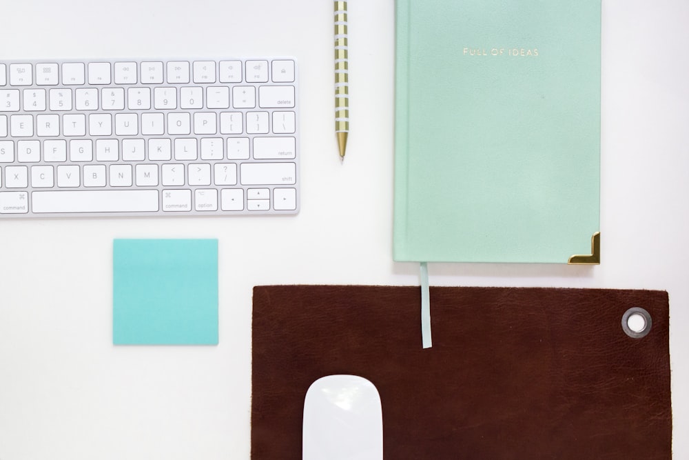 green book beside ballpoint pen and Apple magic keyboard