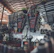A workshop scene features a well-organized wall with an array of tools including wrenches, sockets, and screwdrivers. The tools are neatly arranged and displayed on a metallic surface, with a workbench beneath holding cans of spray and other items. Overhead, beams of the workshop ceiling are visible, providing an industrial backdrop.