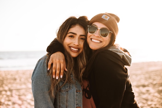 woman hugging other woman while smiling at beach
