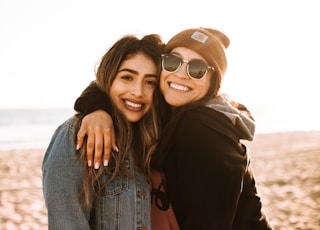 woman hugging other woman while smiling at beach