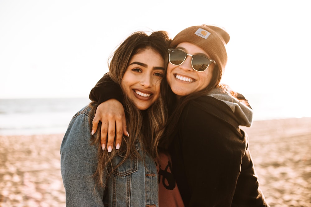 woman hugging other woman while smiling at beach
