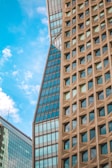 Tall modern skyscrapers with a mix of glass and uniquely textured concrete facades rise against a backdrop of a vibrant blue sky with scattered clouds.