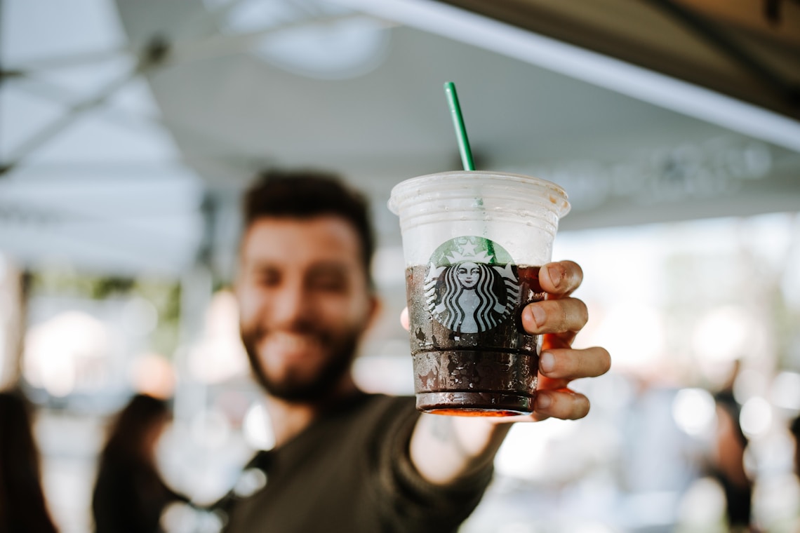 man holding  takeaway Starbucks cup with straw to camera