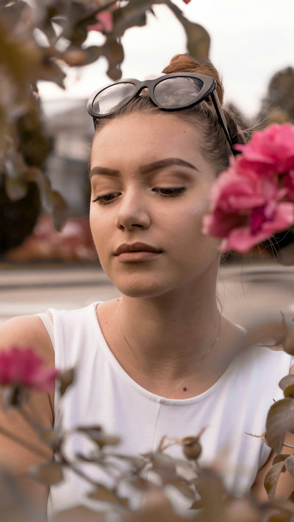 woman wearing white crew-neck sleeveless shirt sitting behind pink petaled flower