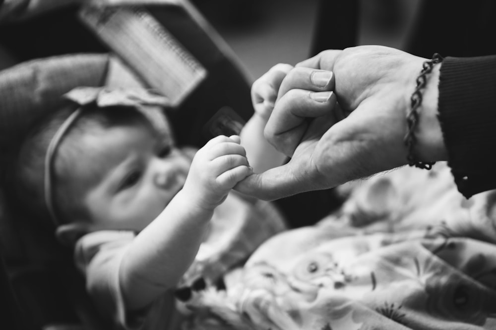 grayscale photo of child holding person finger