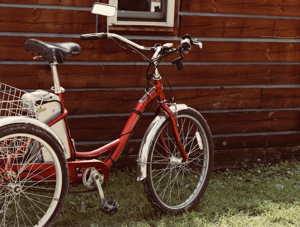 Triciclo rojo para adultos estacionado en posición vertical cerca de la pared