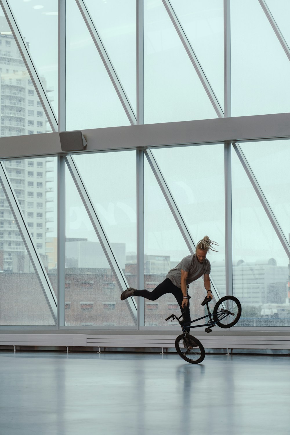 昼間、ガラス張りの建物の中でスタントをする自転車�に乗る男
