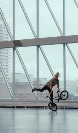 man riding bicycle doing stunts inside glass building during daytime