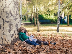 two children sitting on ground with dried leaves