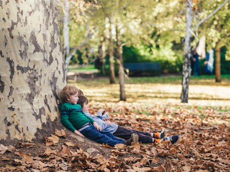 two 7 year old children sitting on ground with dried leaves