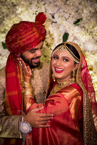 A joyful Indian couple celebrating their wedding surrounded by vibrant maroon and gold decorations.