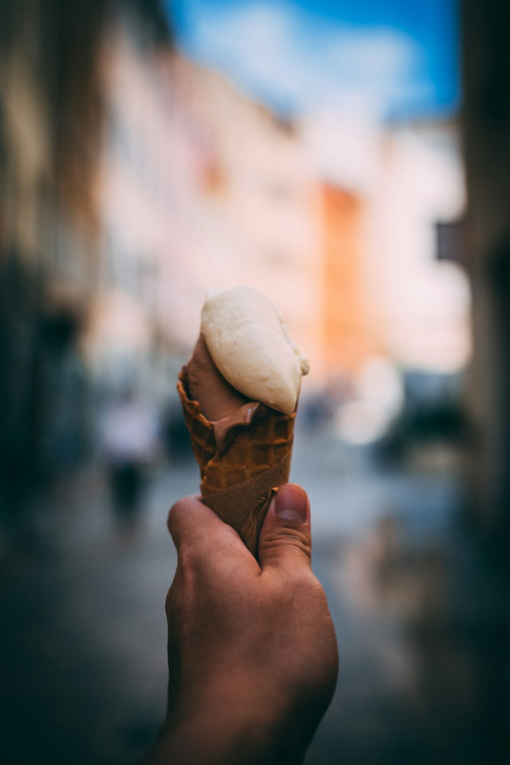 a hand holding an ice cream cone on a city street