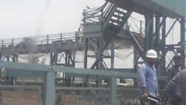A diverse group of skilled workers in hard hats standing proudly in front of a large steel bridge.