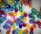 A vibrant array of colorful balloons is attached to the ceiling. These balloons come in shades of blue, purple, yellow, green, and pink, creating a lively and festive atmosphere. Each balloon is tied with a string, contributing to the overall aesthetic.