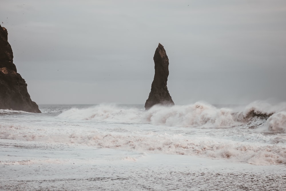 ocean waves move near rock formation under cloudy sky