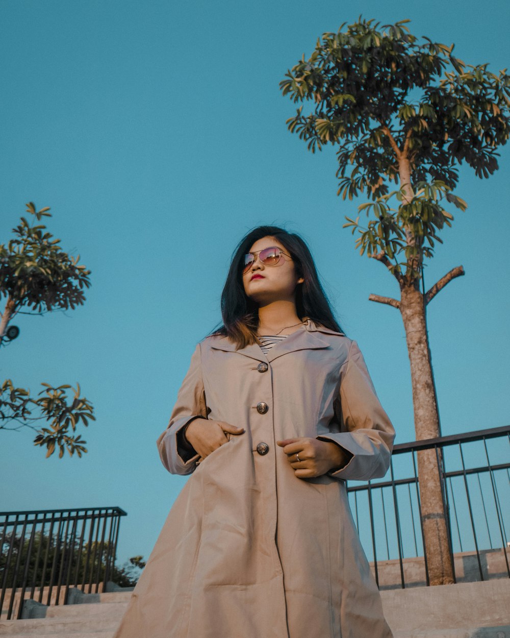 woman in gray overcoat near green leafed tree during daytime low angle photography