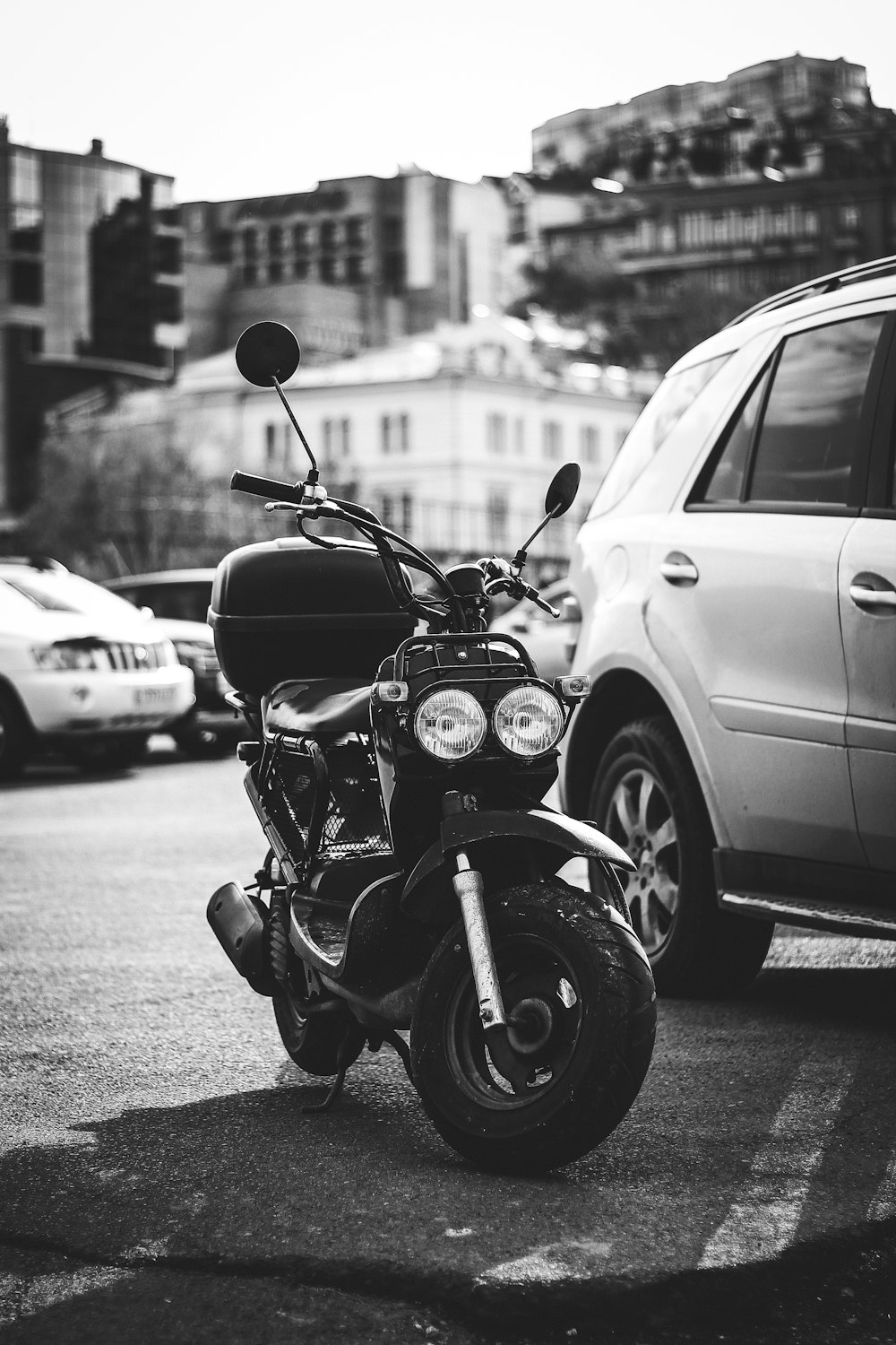 grayscale photography of scooter beside car