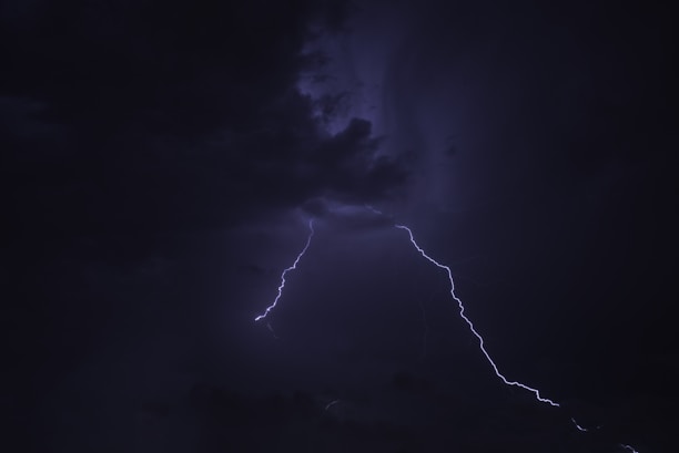 Dark stormy sky with bright lightning bolt cutting through the clouds, creating a dramatic and intense atmosphere.