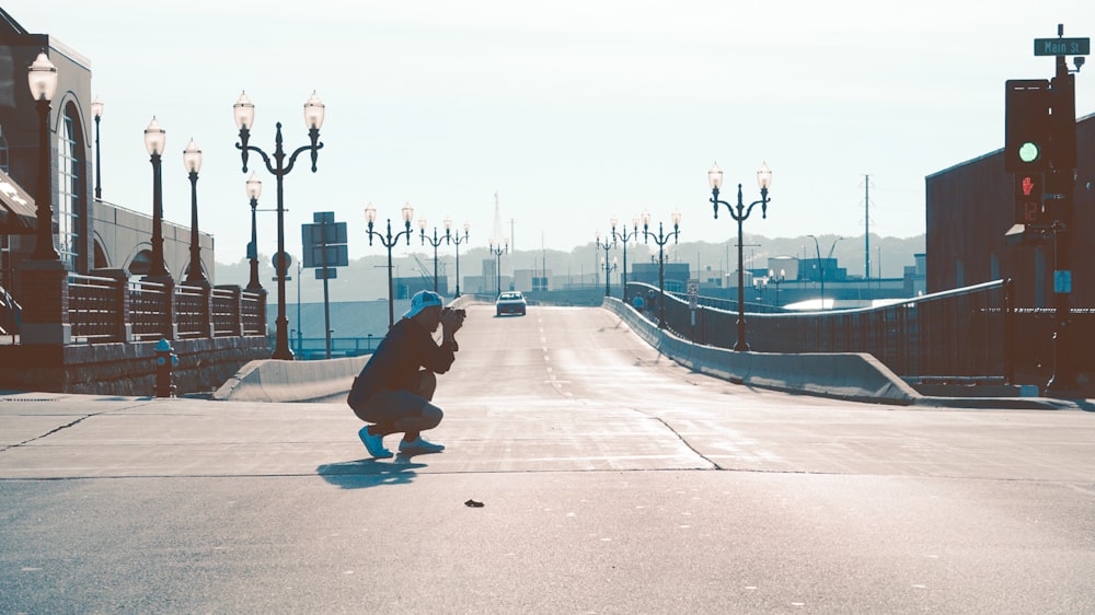 man squatting on road while taking photo