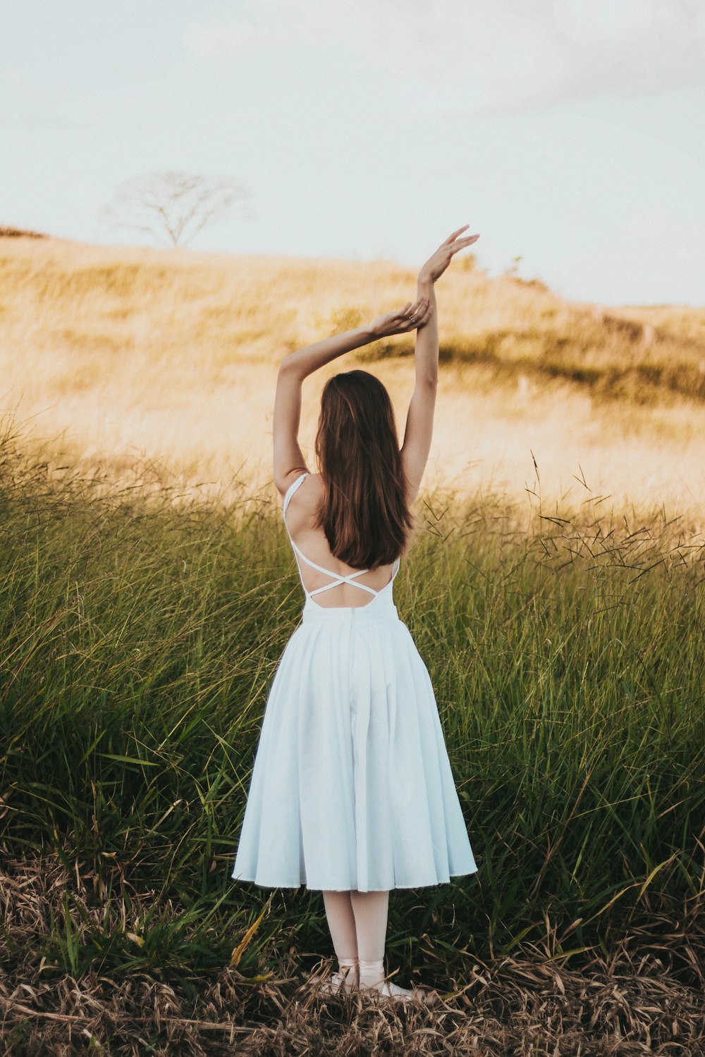 donna che indossa un vestito bianco senza maniche in piedi vicino all'erba durante il giorno