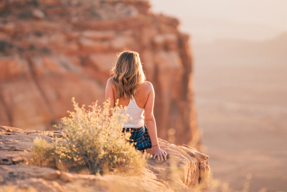 woman sitting on cliff during daytime