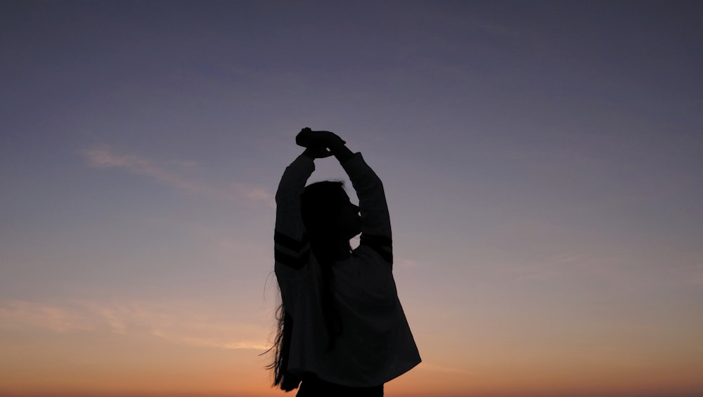 a silhouette of a person holding a cell phone up in the air