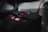 A close-up view of a sleek, black gaming mouse with red accents and buttons. The mouse design includes a textured grip and a scroll wheel, with a coiled wire partially visible in the background.