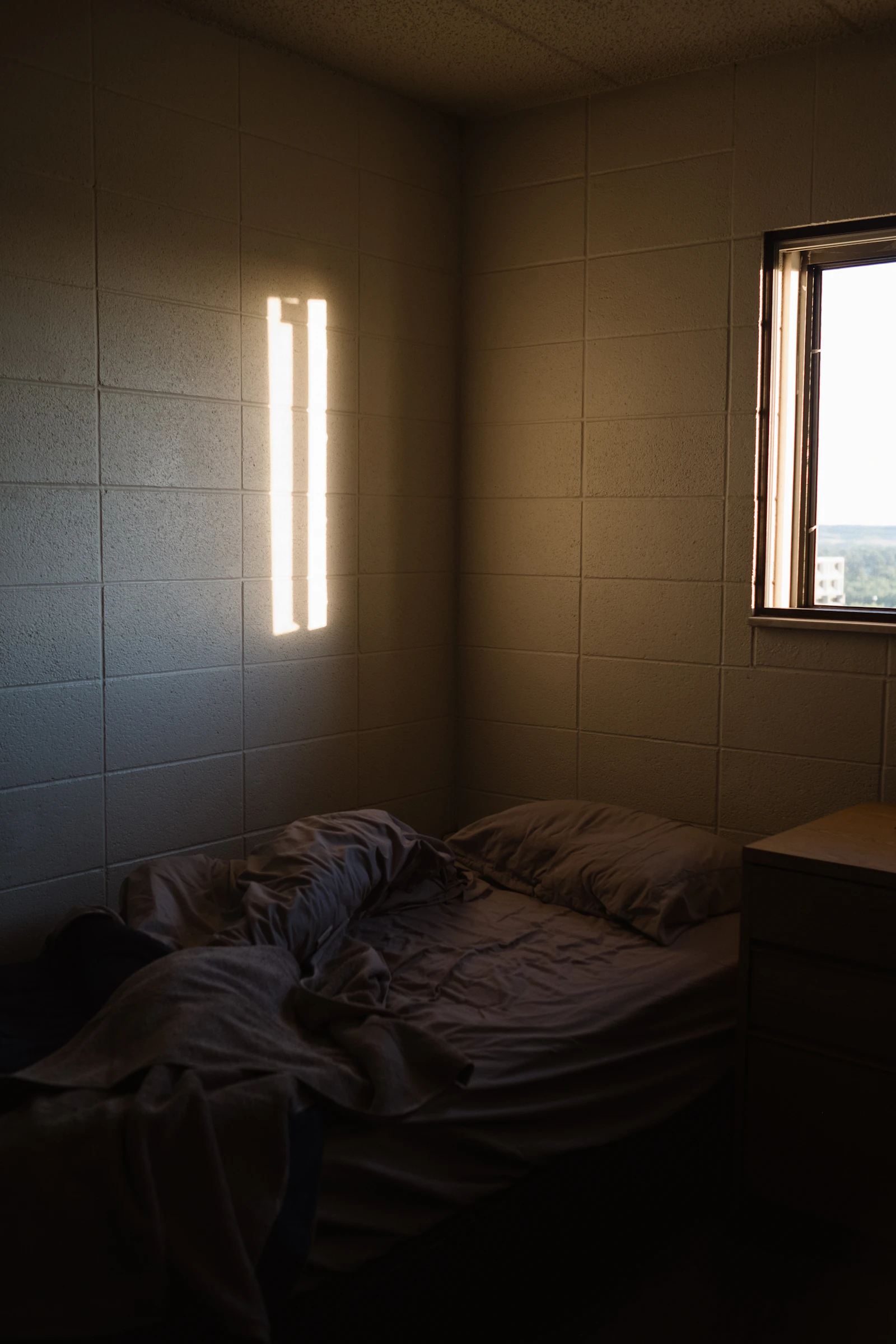 unmade bed in a cinder block dorm room