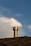 A friendly chimney technician inspecting a chimney cap on a sunny Ventura rooftop.