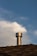 A metallic chimney vent extends from the peak of a shingled roof against a backdrop of a partly cloudy sky. The texture of the roof shingles is visible, and the chimney vent reflects light, giving it a metallic sheen.