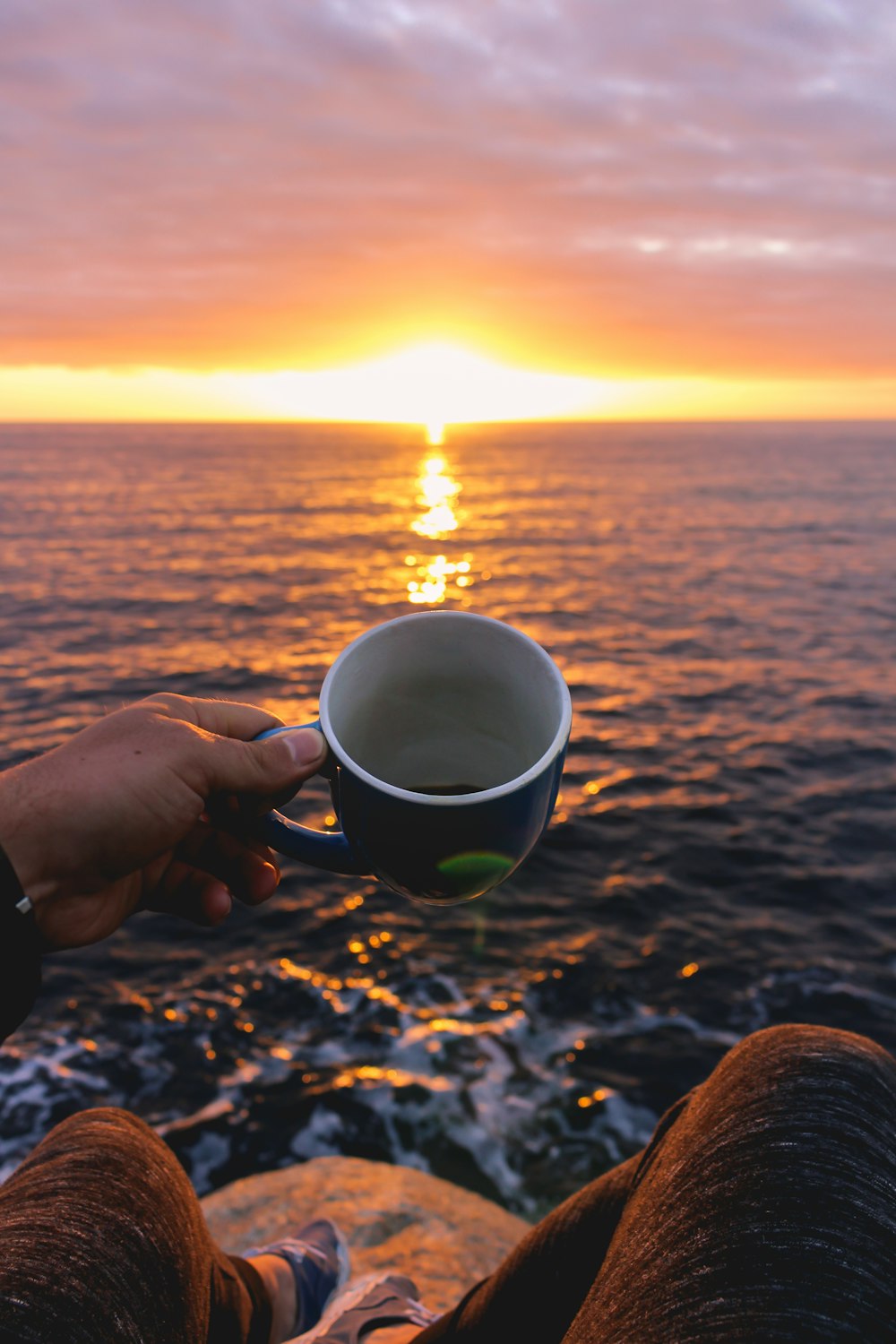 person holding blue cup looking at sunset