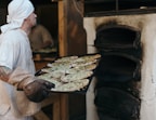 A baker spreading garlic butter on naan before baking.