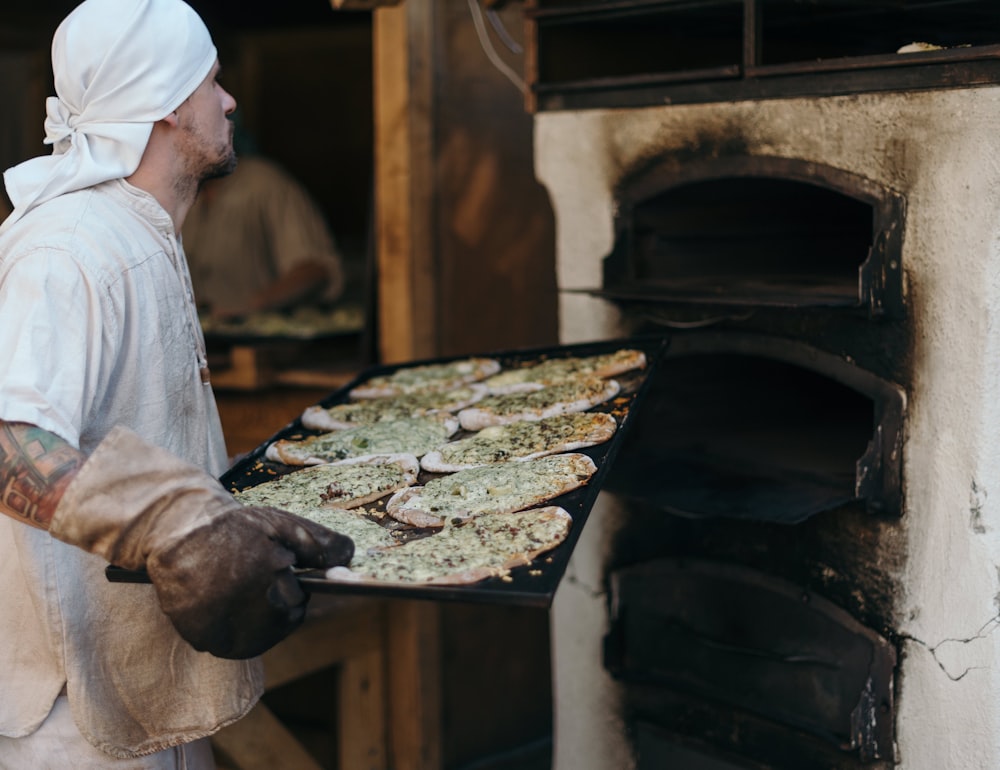 a man holding a tray of food in front of an oven