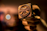 A hand holding a close-up view of a metal stamp with a rustic, worn appearance. The stamp features text and symbols, likely used for branding or decorative purposes. The background is blurred with warm tones, enhancing the focus on the stamp.