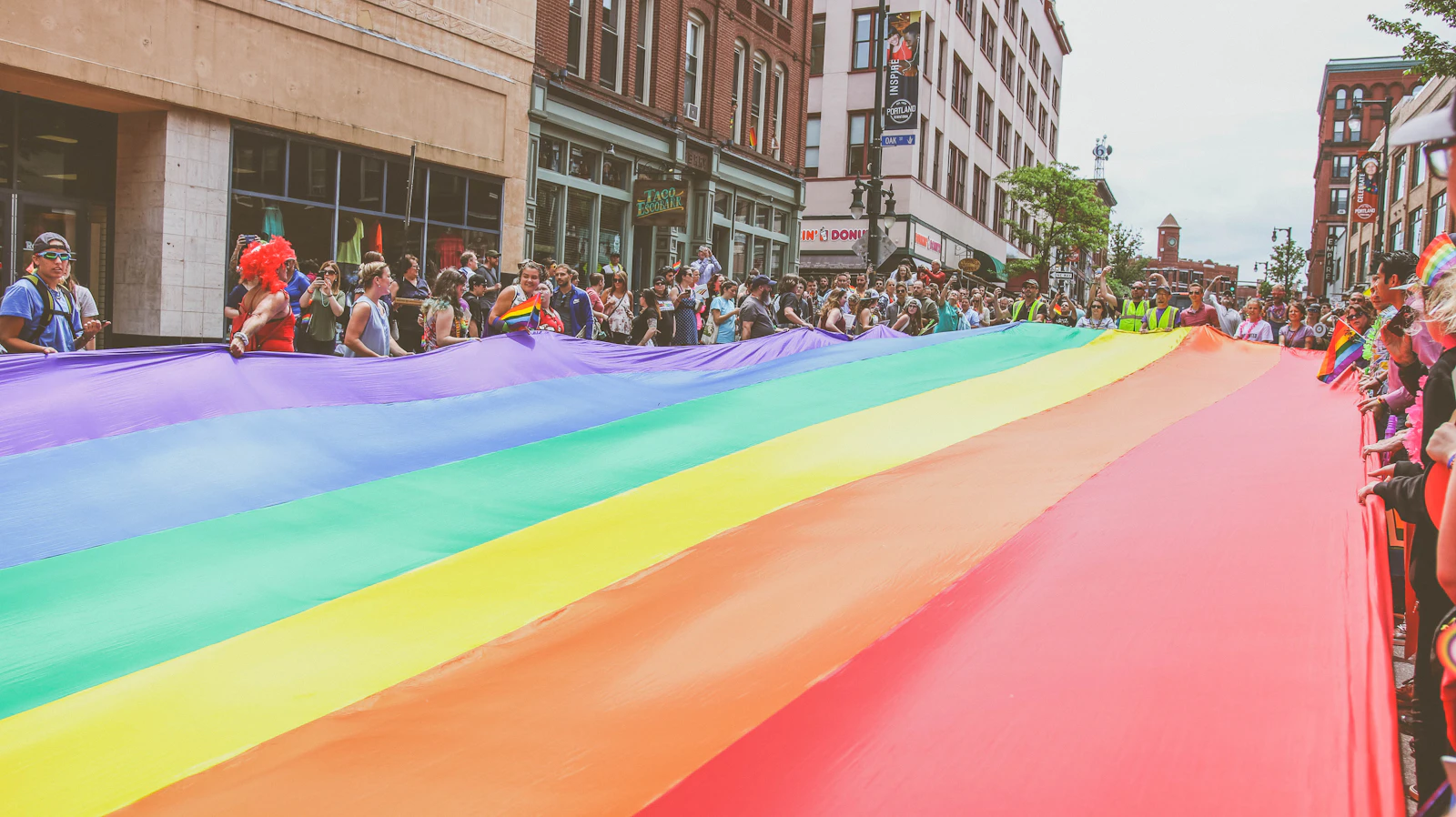 A crowd carries a large rainbow flag down the street during a Pride parade