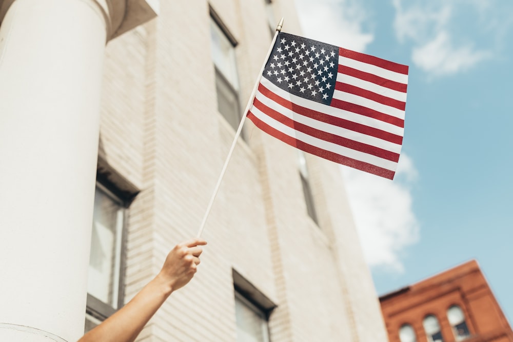 Eine Person, die eine amerikanische Flagge vor einem Gebäude hält