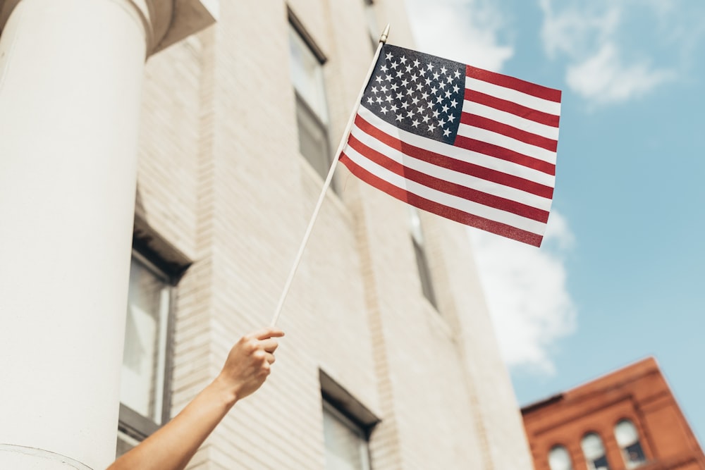 Una persona sosteniendo una bandera estadounidense frente a un edificio
