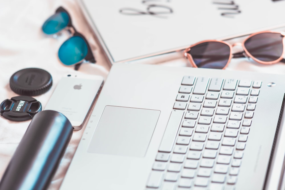 laptop, iPhone, and sunglasses on table