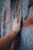 Hands holding a freshly cut stencil sheet against a graffiti-covered wall.