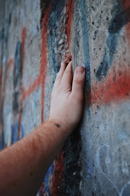Hands holding a freshly cut stencil sheet against a graffiti-covered wall.