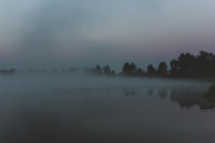 A misty lake at dawn with a mysterious silhouette barely visible on the water.