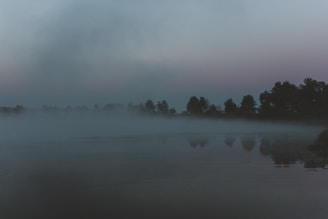 A misty lake at dawn with a mysterious silhouette barely visible on the water.