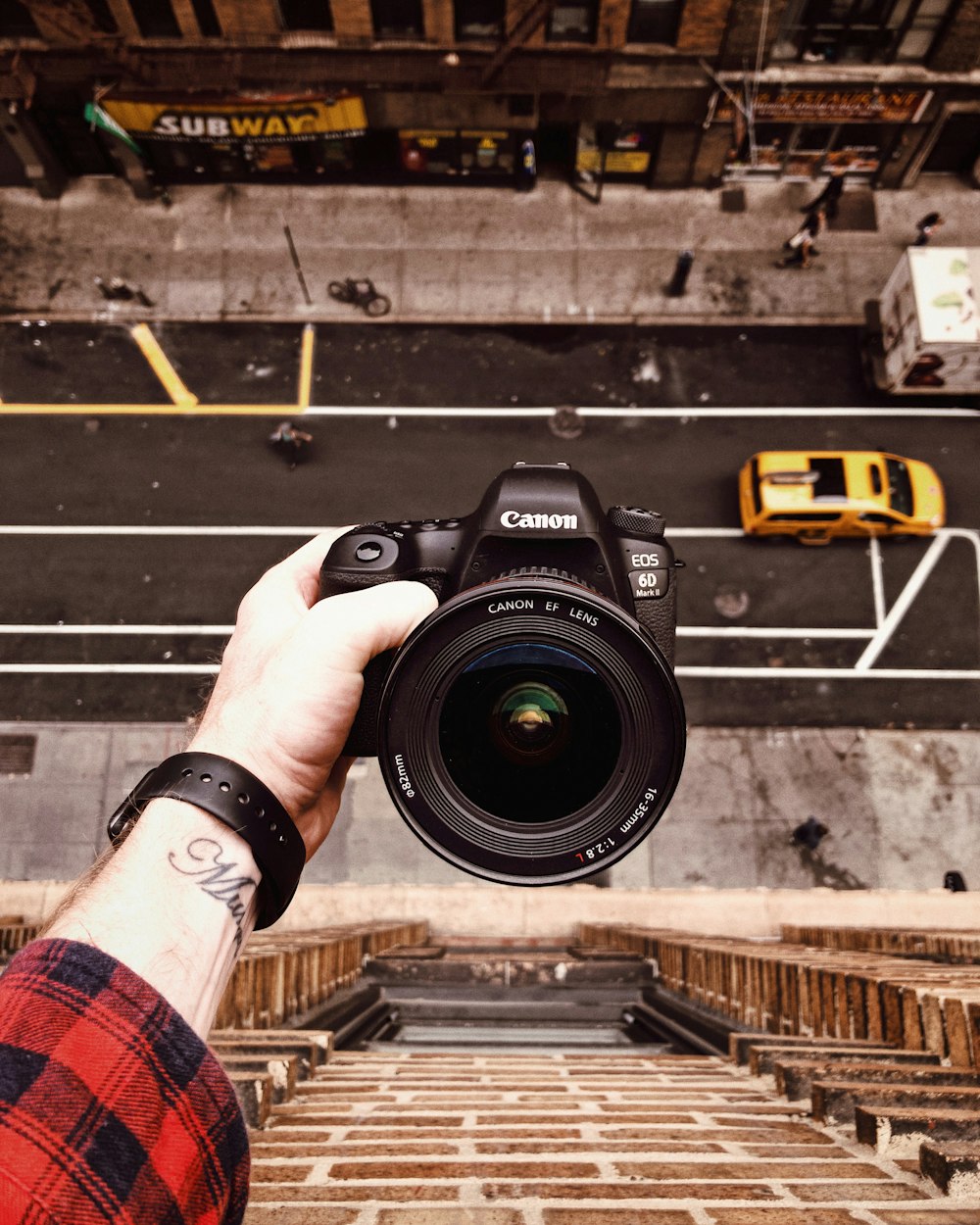 person holding black Canon EOS 6D outside window