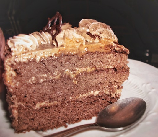 A decadent chocolate cake slice with rich frosting and a sprinkle of powdered sugar on a white plate.